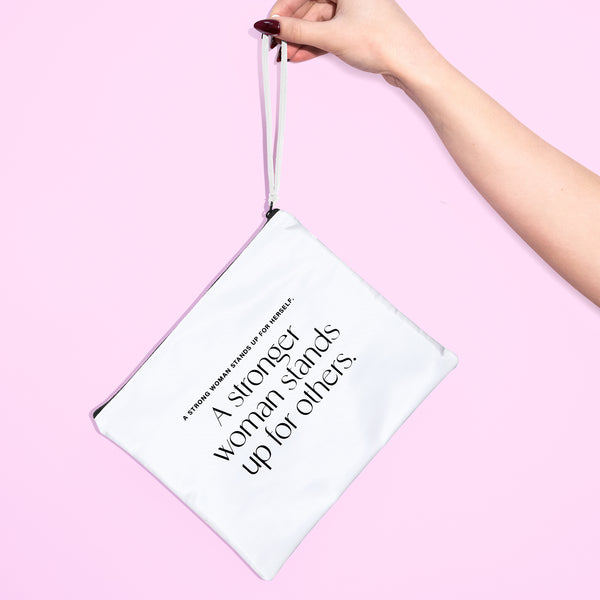 A hand holding a white bag that says "A strong woman stands up for herself. A stronger woman stands up for others." on a pink background