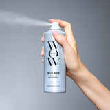 Hand holding silver Color Wow Insta-Wow Advanced Dry Shampoo spray can, 171ml / 142g / NET WT 5.0oz, releasing mist against a neutral gray background.
