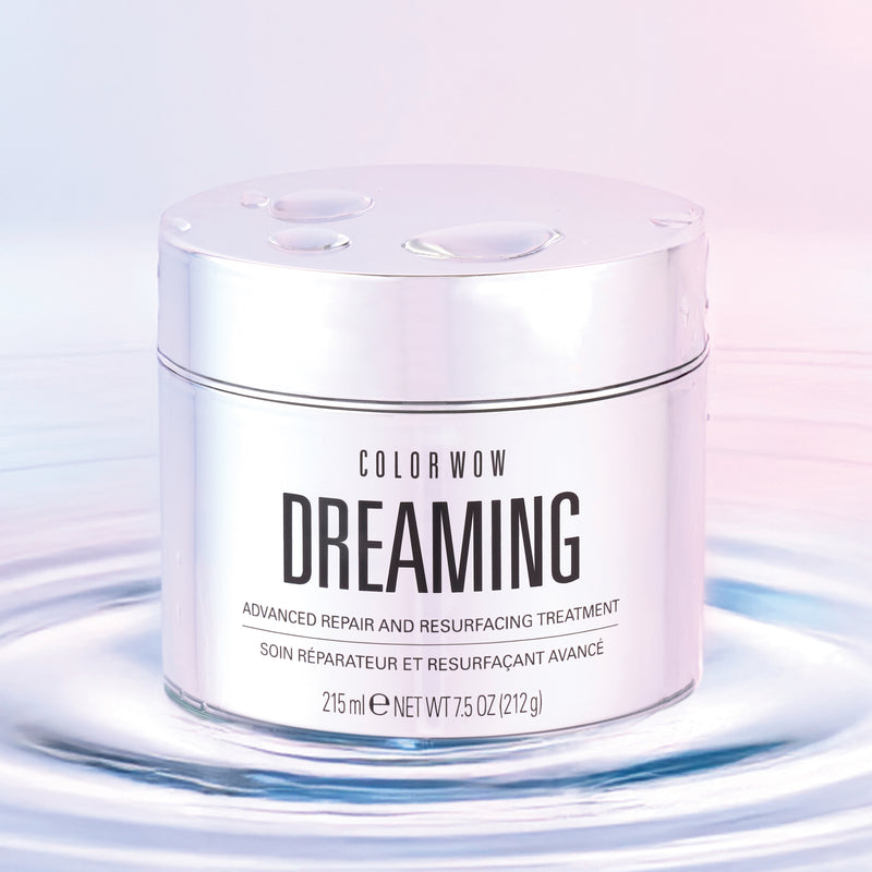 Color Wow Dreaming Advanced Repair and Resurfacing Treatment in a sleek, reflective silver jar, set against a soft gradient pink and blue background with water droplets on the lid, emphasizing its hydrating and restorative hair benefits.